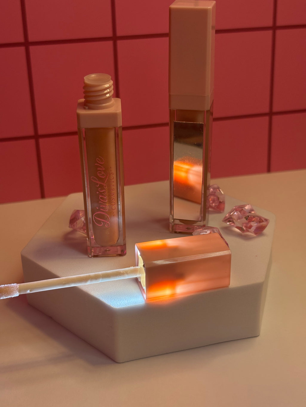 Diva's Elegance light nude lip gloss by Diva's Love Cosmetics, open with applicator displayed on white platform with mirror and pink crystals