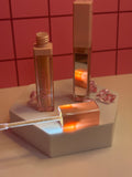 Diva's Elegance light nude lip gloss by Diva's Love Cosmetics, open with applicator displayed on white platform with mirror and pink crystals