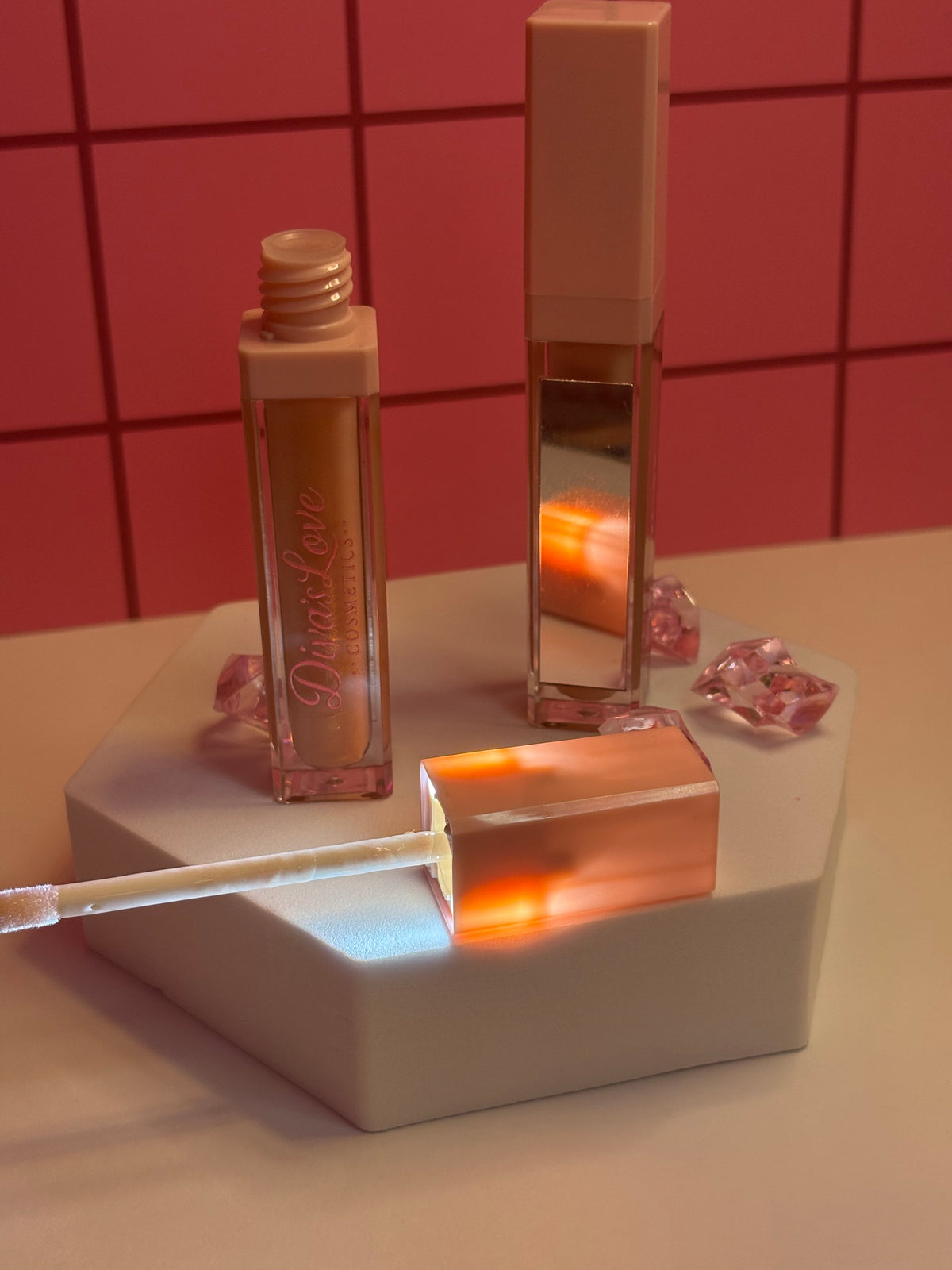 Diva's Elegance light nude lip gloss by Diva's Love Cosmetics, open with applicator displayed on white platform with mirror and pink crystals