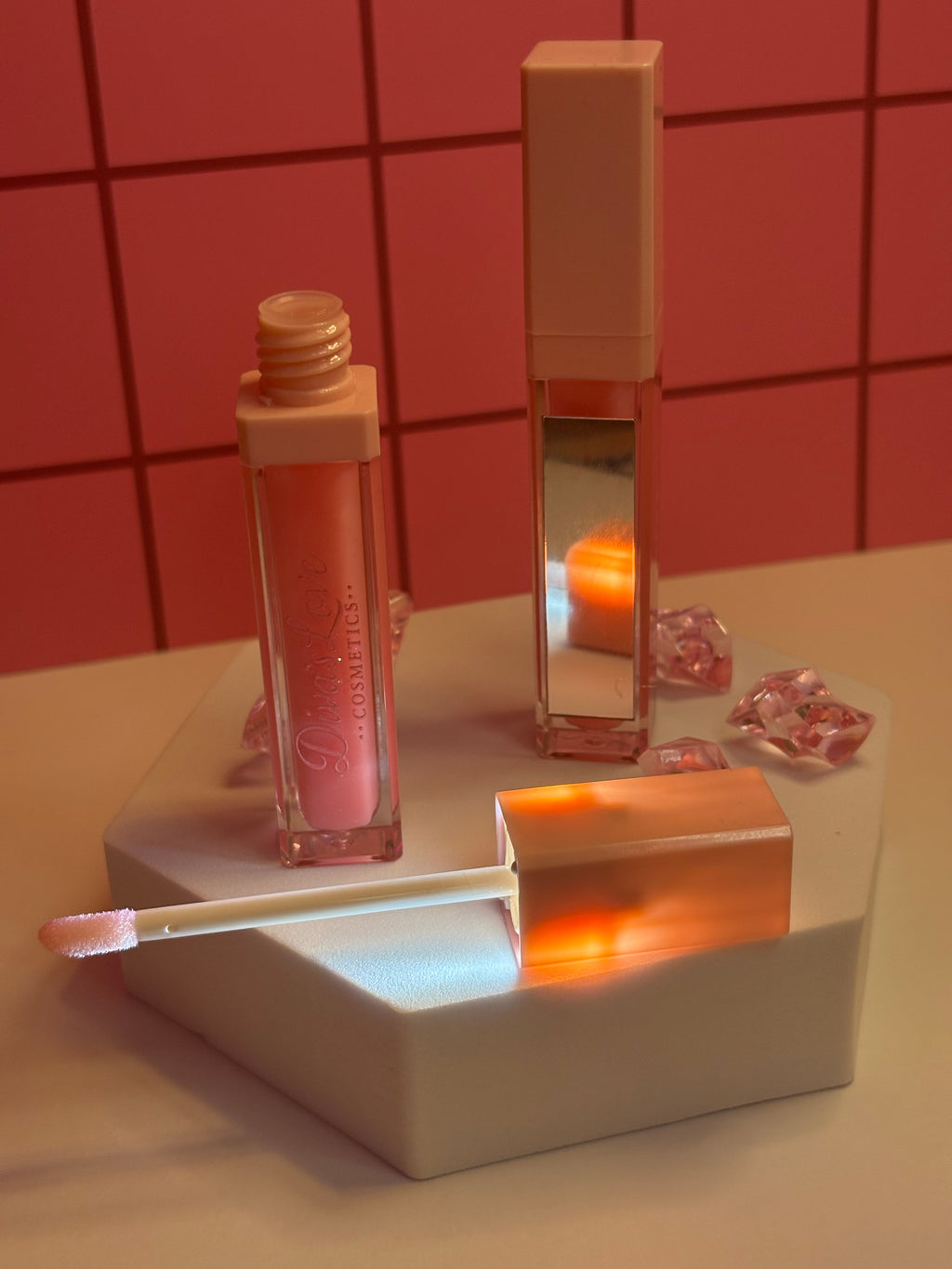 Princess Diva soft pink lip gloss by Diva's Love Cosmetics, open with applicator displayed on white platform with mirror and pink crystals