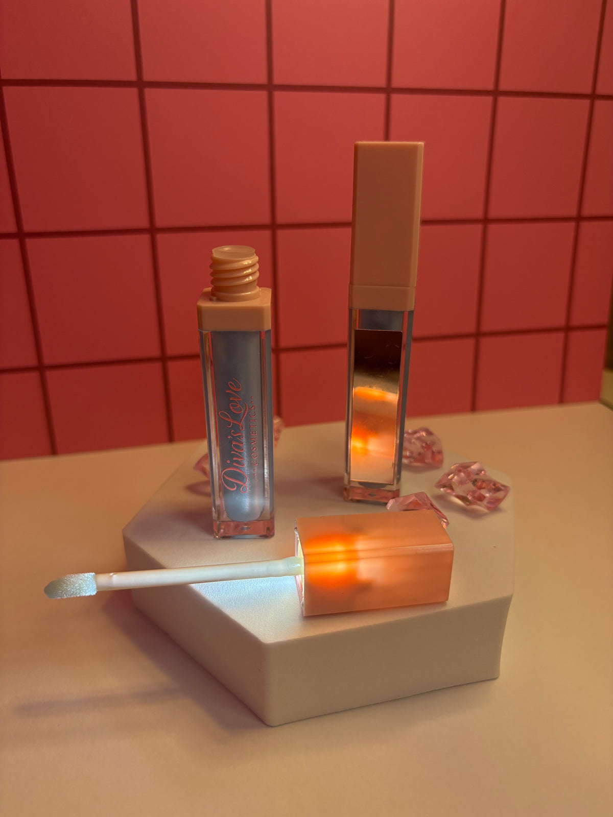 Diva's Sky cool blue-grey lip gloss by Diva's Love Cosmetics, open with applicator displayed on white platform with mirror and pink crystals