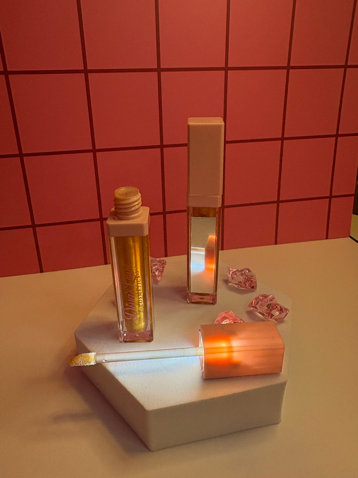 Diva's Gold rich gold lip gloss by Diva's Love Cosmetics, open with applicator displayed on white platform with mirror and pink crystals